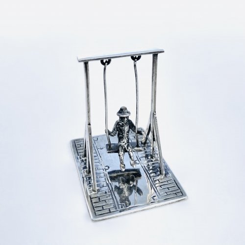 Miniature silver model of man on a swing.